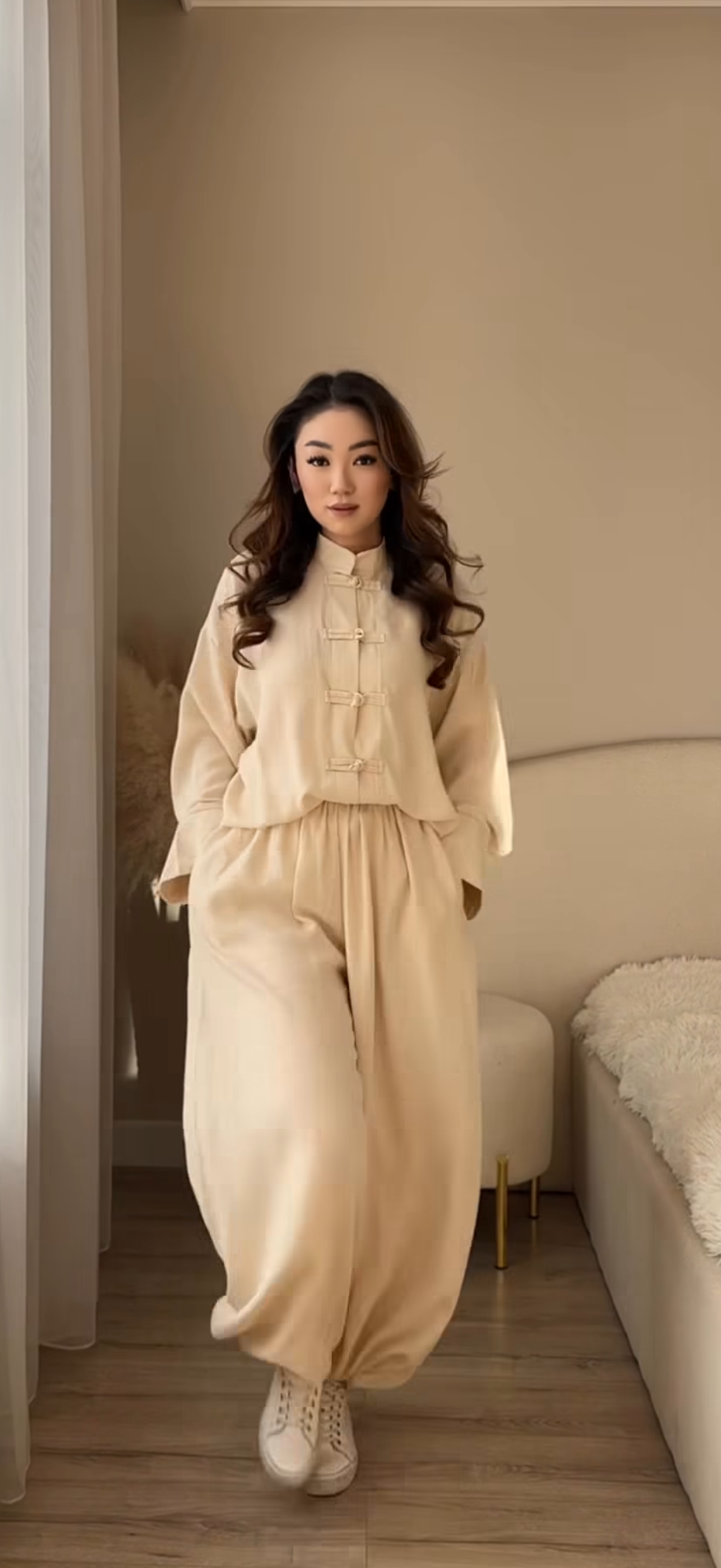 Woman in a beige outfit standing in a room with neutral decor.